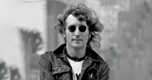 John Lennon cu ochelari rotunzi și geacă denim, portret alb-negru