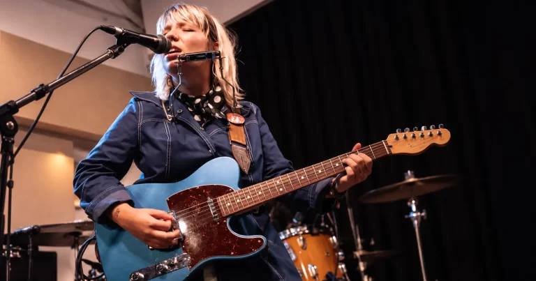 Lily Seabird cântând la chitară electrică și muzicuță în timpul unui concert.