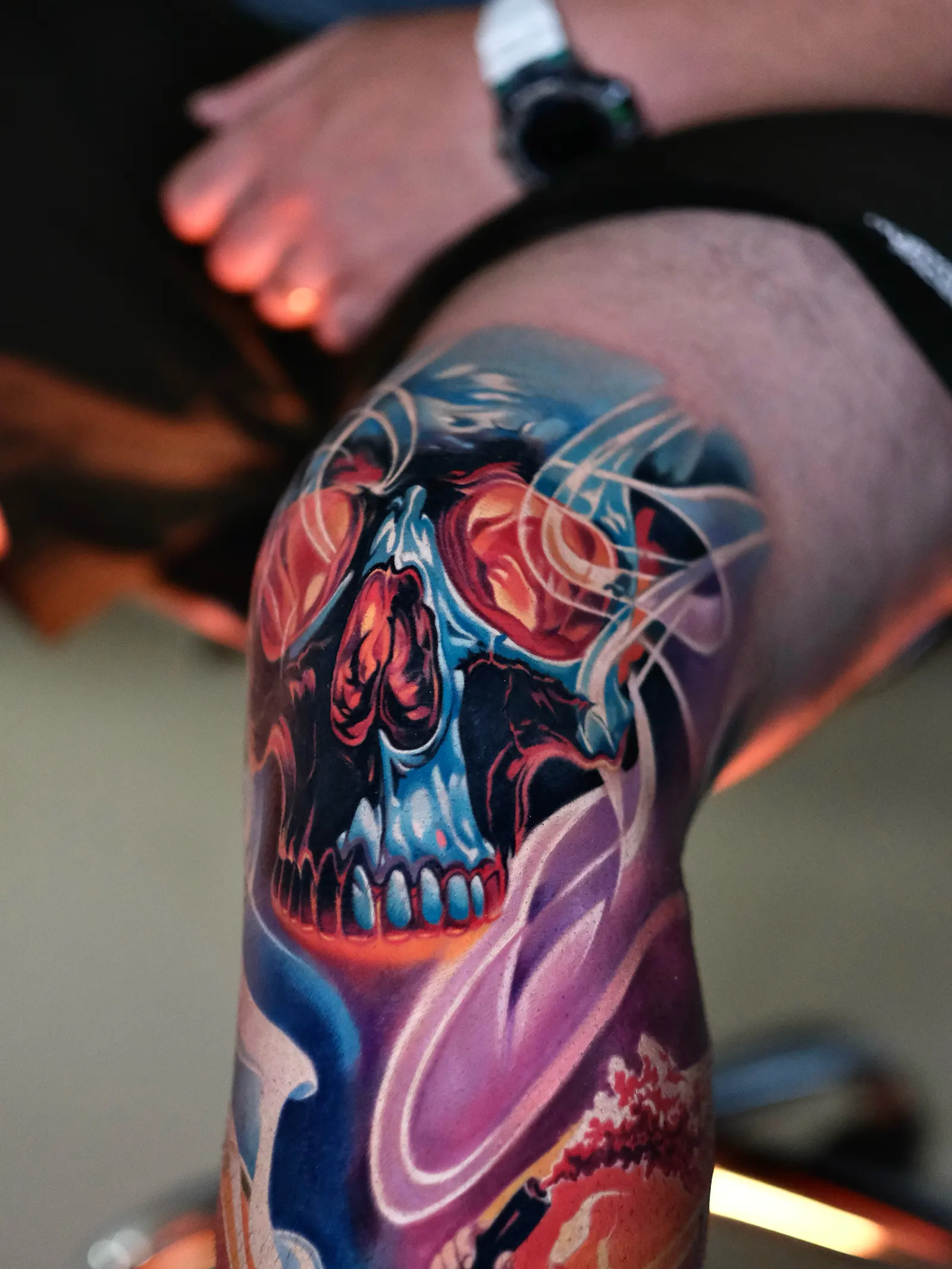 Tatuaj color cu craniu stilizat, în nuanțe de albastru, roșu și violet.