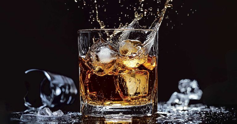 Cocktailuri cu whisky și cuburi de gheață, într-un pahar cu băutură ambrată
