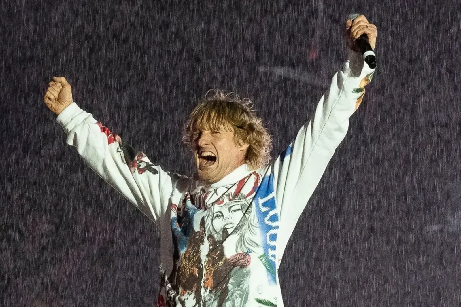 Owen Wilson cu brațele ridicate în ploaie, într-o scenă din Rolling Loud